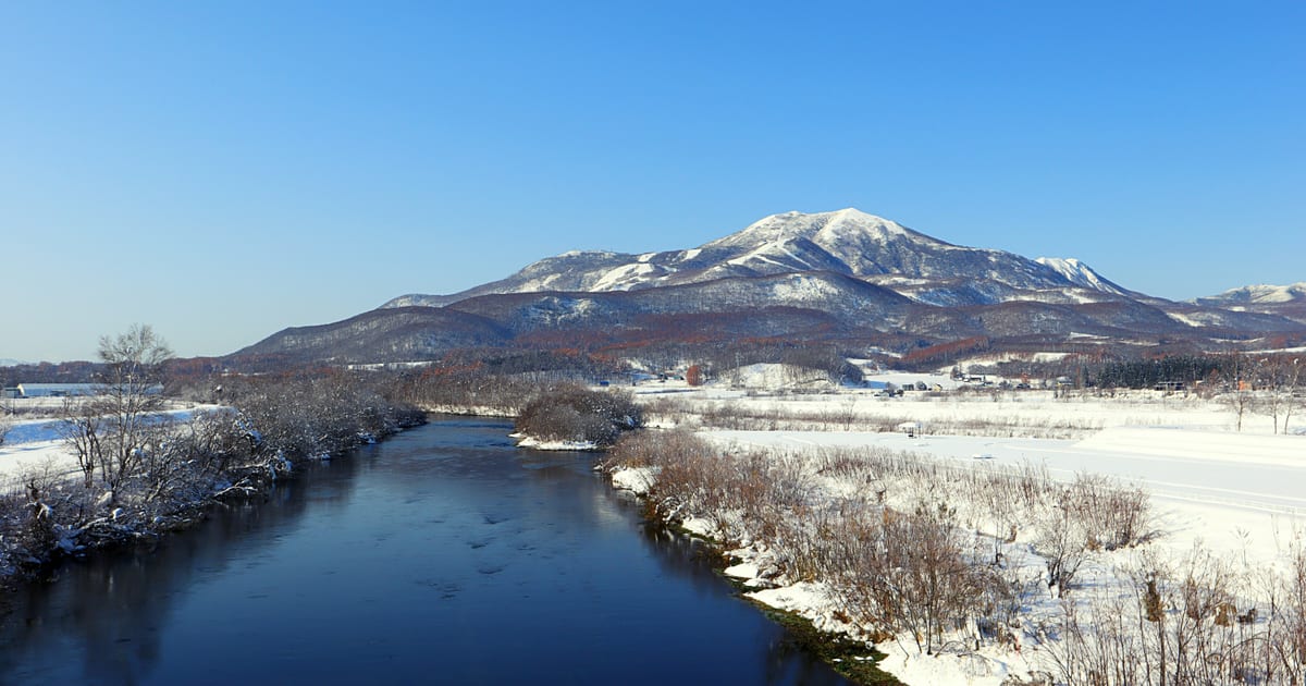 Niseko Annupuri nevado visto desde Kutchan en un día de invierno despejado, con un río y campos nevados en primer plano