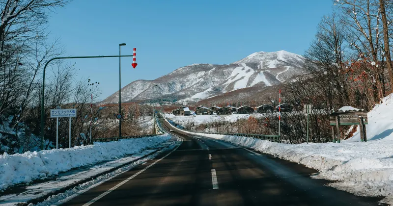 Snow-lined road leading to the Hirafu ski area in Niseko, with snow-capped mountains ahead