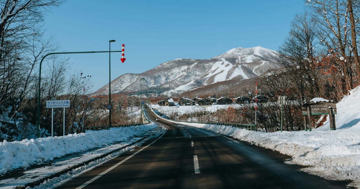 Snow-lined road leading to the Hirafu ski area in Niseko, with snow-capped mountains ahead
